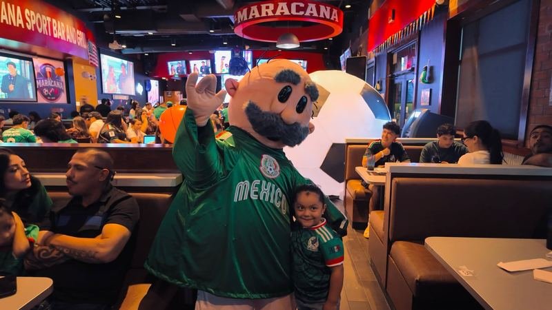 Match Day Mascot: The Mexico-jersey mascot poses with fans in a packed house.