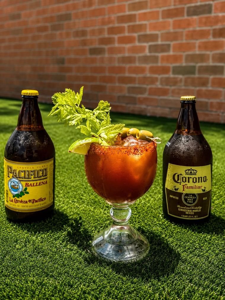 Bloody Maria cocktail with celery, olives and lime, flanked by Pacifico and Corona bottles